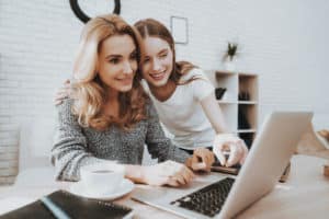 Mother and Daughter Watching into Laptop at Home. Daughter Helping Mother. Mother and Daughter at Home. Teenage Girl. Frilancing Mother Concept. Women Using Digital Device. Smiling Woman.